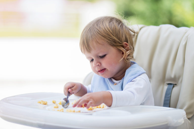 baby boy feeding himself eggs in a highchair