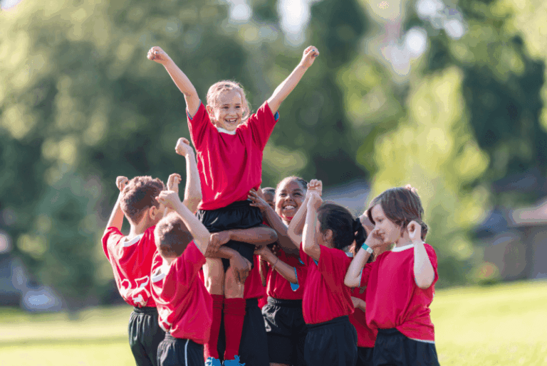side view of a bunch of kids cheering each other on for a sports event and lifting one another up