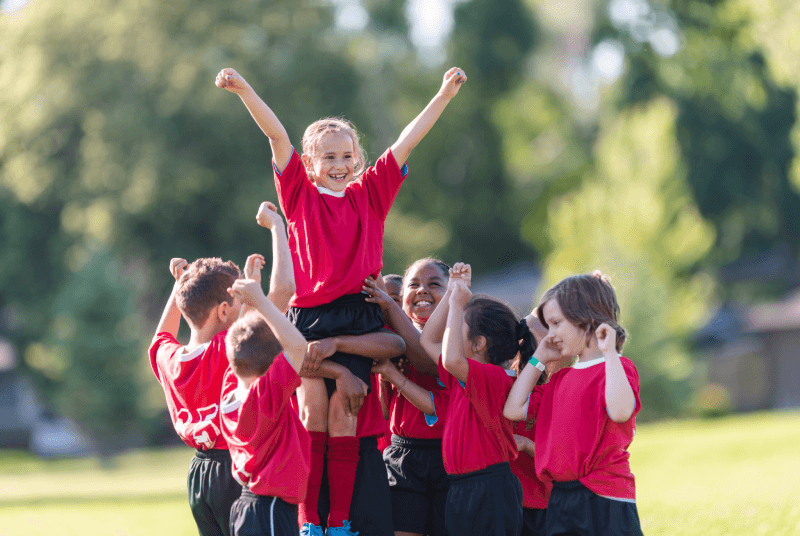 side view of a bunch of kids cheering each other on for a sports event and lifting one another up