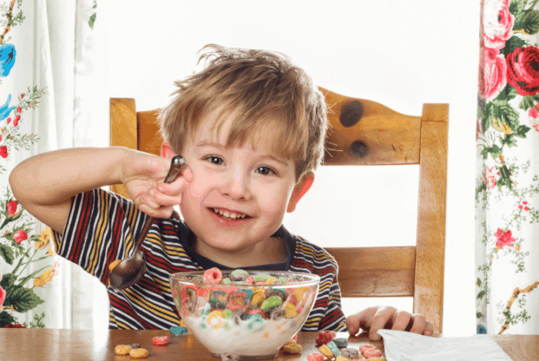 A smiling child with ADHD eats a bowl of fruity cereal facing the camera