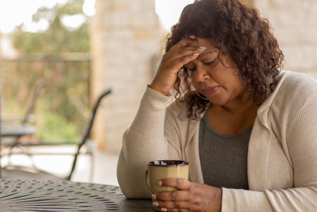 A stressed out women with her hand on her forehead with a cup of tea