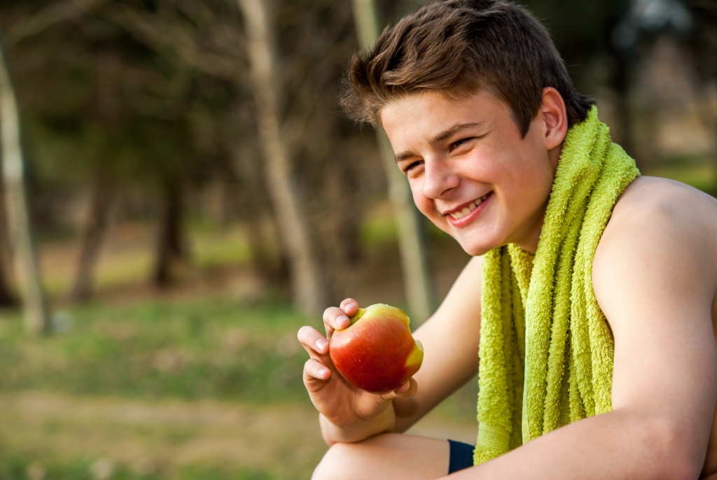 close up of a smiling teen boy holding an apple just after he completed a sports practice