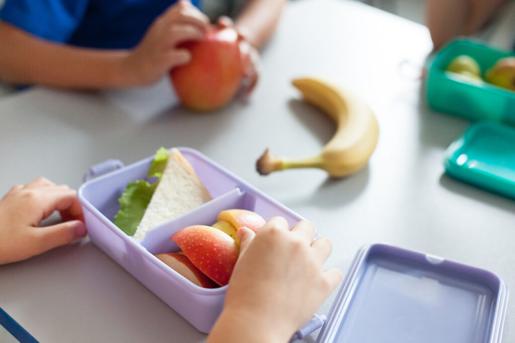 School kids eating school lunch ideas for picky eaters from packed lunch boxes. Children sit at table in cafeteria. Pupils have vegetarian breakfast in canteen. Back to school concept. Lifestyle moment in elementary college