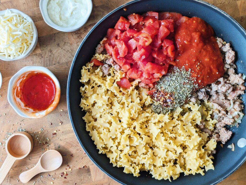 uncooked pasta in skillet with cooked meat
