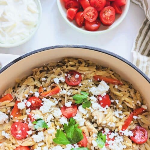 One-pan Mediterranean chicken and veggie orzo topped with tomatoes, olives, feta, and tzatziki.