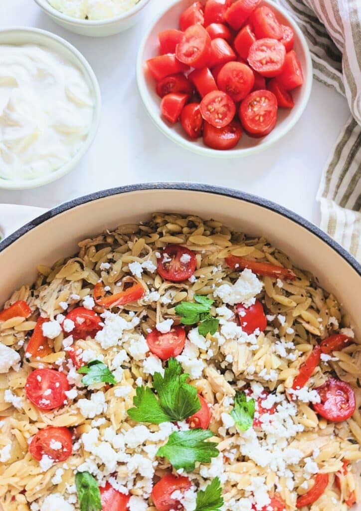One-pan Mediterranean chicken and veggie orzo topped with tomatoes, olives, feta, and tzatziki.