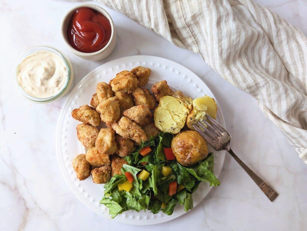 top view of air fryer chicken nuggets on a plate with a salad and bread
