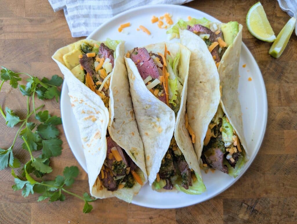 three flank steak tacos on a plate with all the fixings