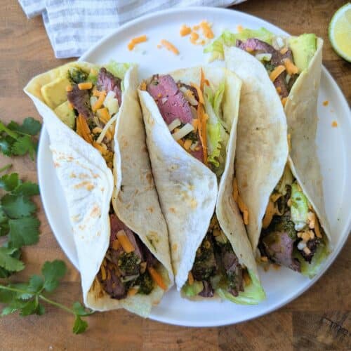 three flank steak tacos on a plate with all the fixings