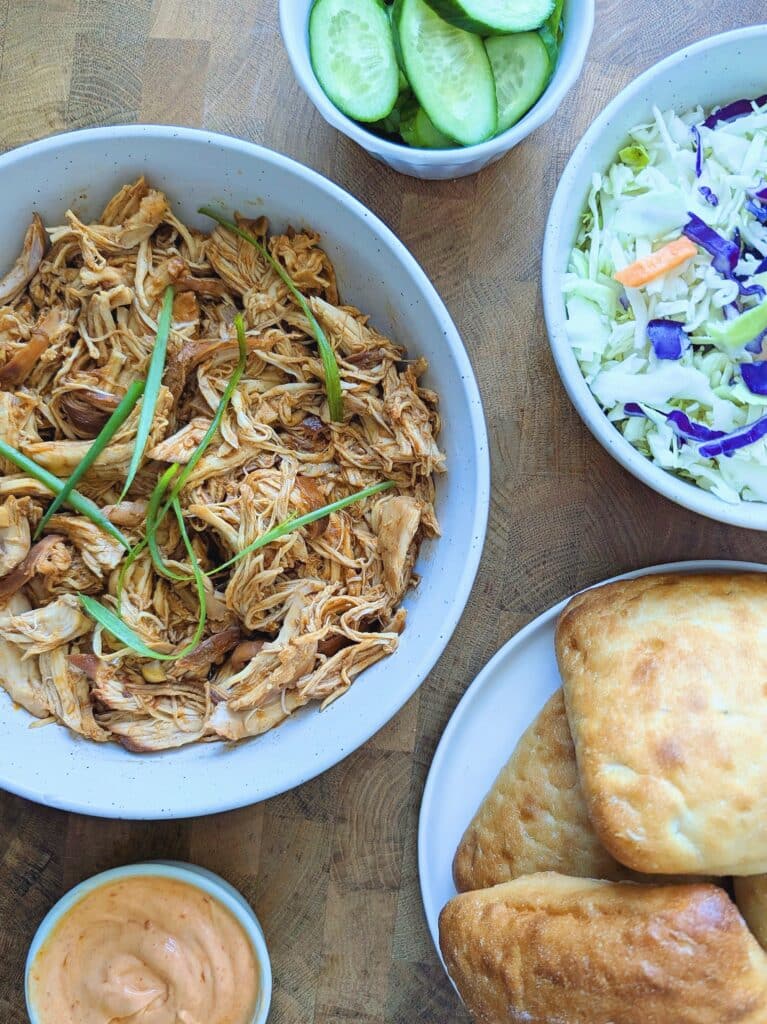 top-down view of ingredients needed to make these slow cooker gochujang chicken sandwiches, including shredded chicken, buns, and salad