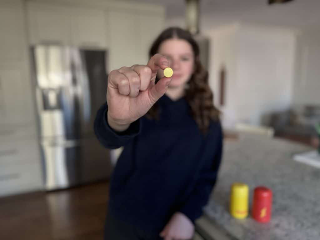 a teen girl holding a chewable vitamin close to the camera