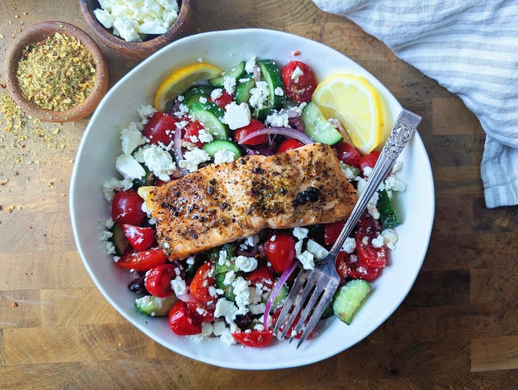 top down view of air fryer Greek salmon over top of a salad in a bowl