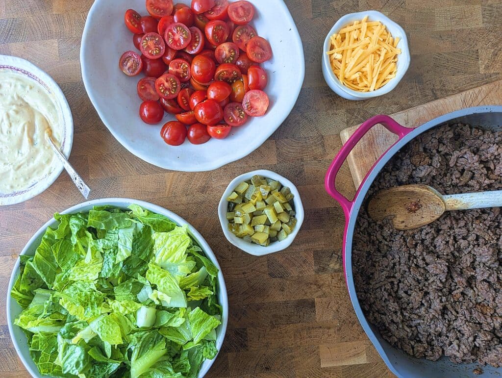 ingredients needed to prep the cheeseburger salad bowls including tomatoes, lettuce, cheese