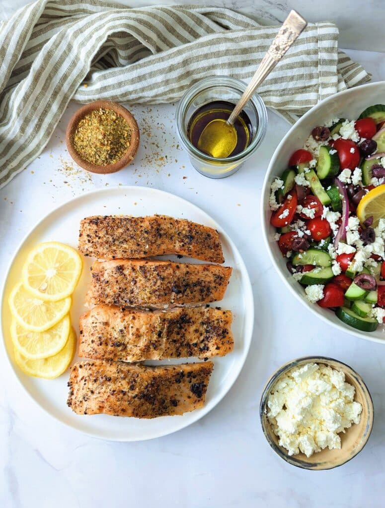 vertical shot of air fryer Greek salmon with ingredients to assemble Greek salad