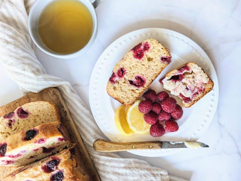 top down raspberry lemon loaf in slices with butter on a white plate topped with raspberries and lemon slices