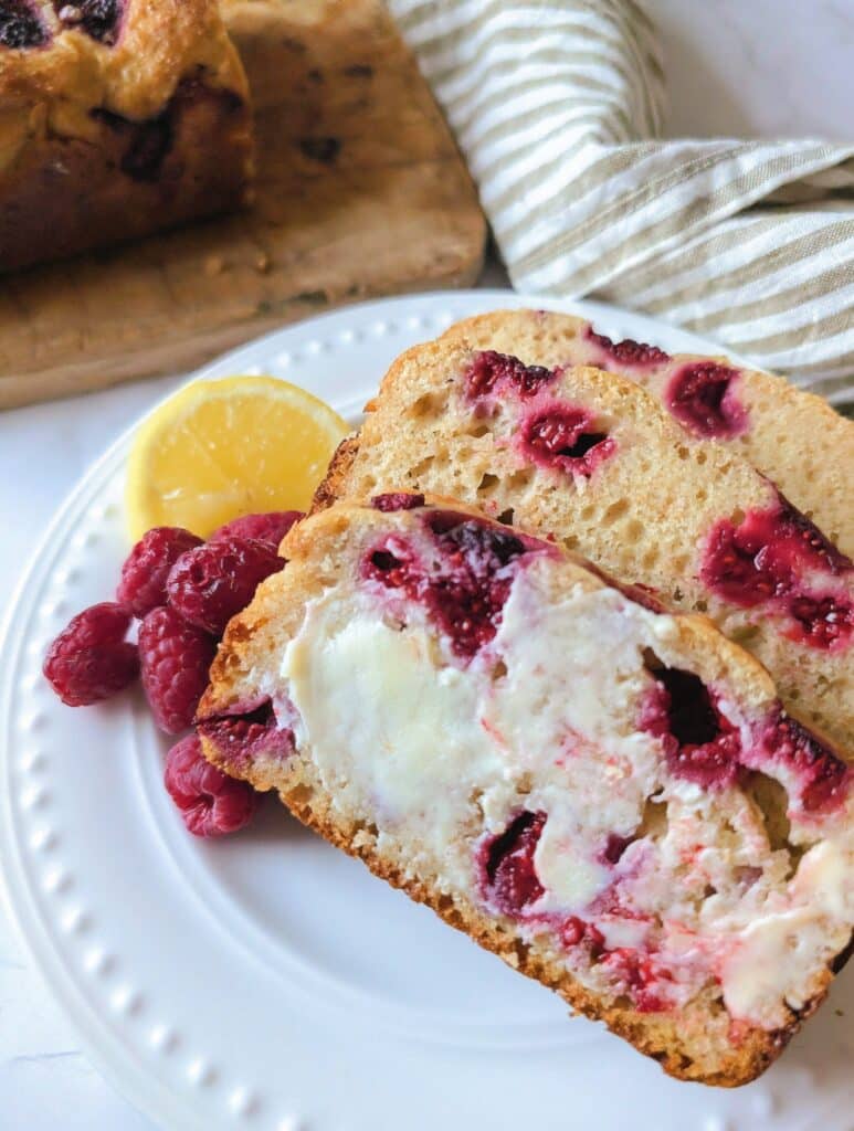 side view of raspberry lemon loaf in slices topped with butter on a plate