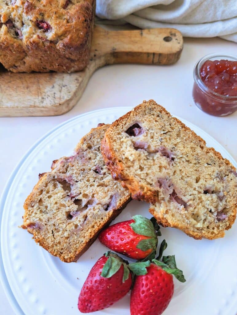 side view of strawberry snacking loaf on a plate with fresh strawberries
