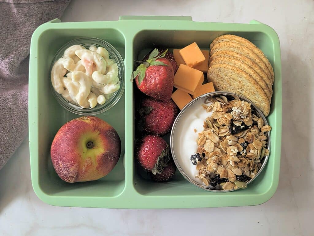 top down view of air fryer granola in a school lunch box with fruit and cheese