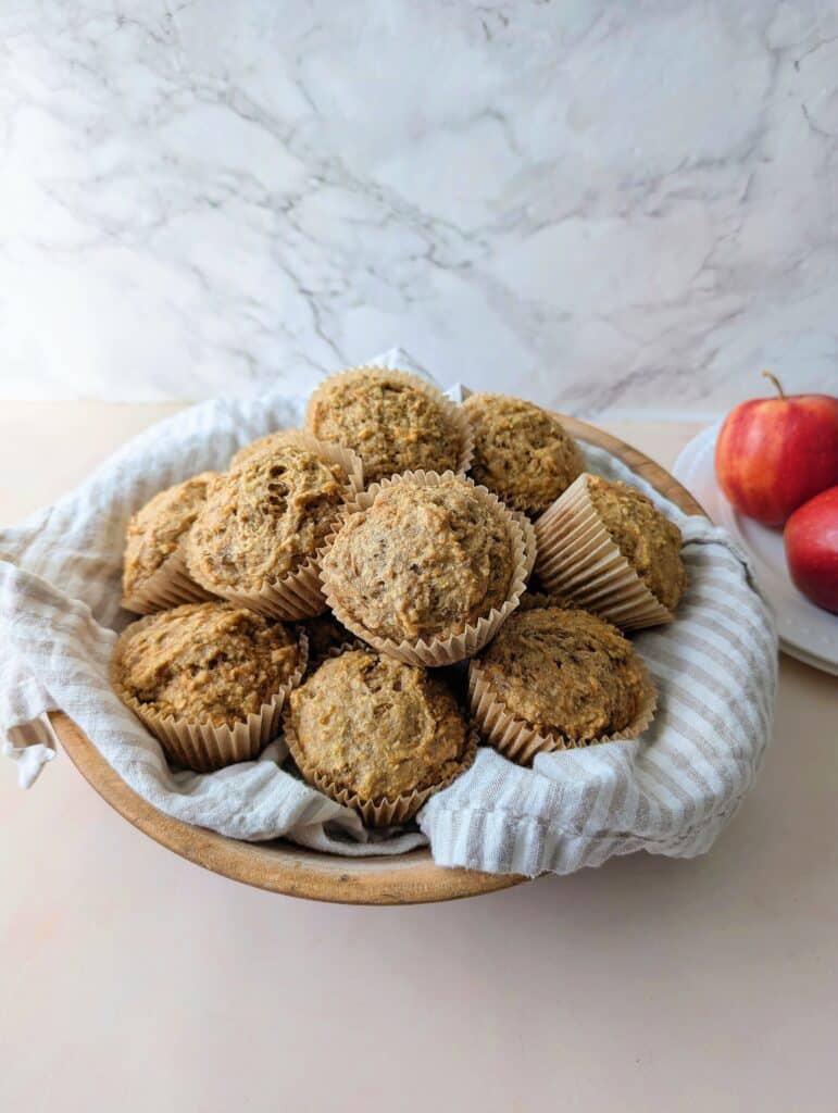 close up of muffins in a bowl with apples in the background